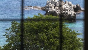 A rocky island surrounded by clear blue water, viewed through a window with a grid pattern. - Palia Damouchari (Zagora-Mouresi)
