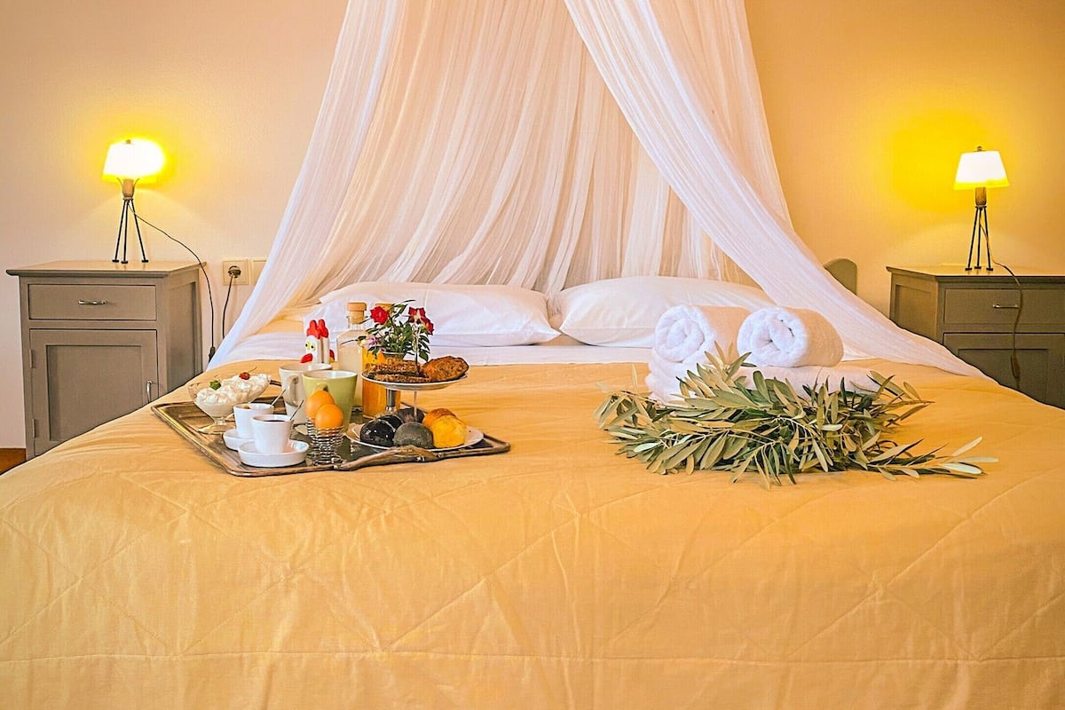 Een keurig opgemaakt bed met hemelbed, nachtkastjes met lampen, en een dienblad met ontbijtartikelen.