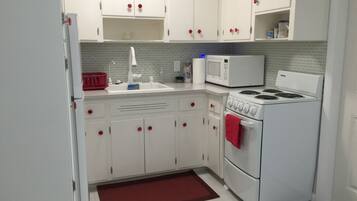A compact kitchen with white cabinets, a white stove, a microwave, and a red towel hanging on the oven.