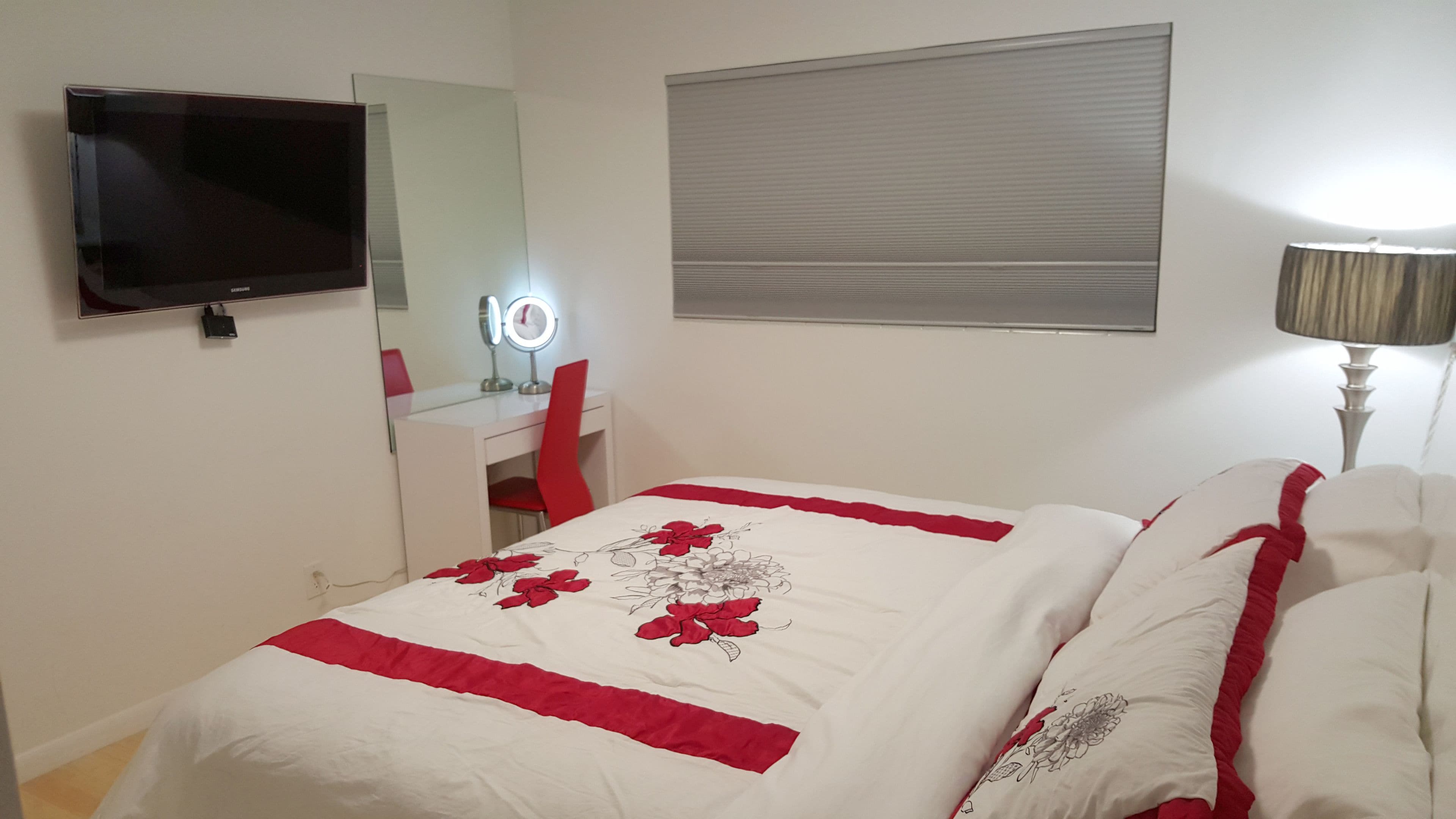 Un dormitorio con una cama, un televisor, un tocador con espejo y una lámpara.