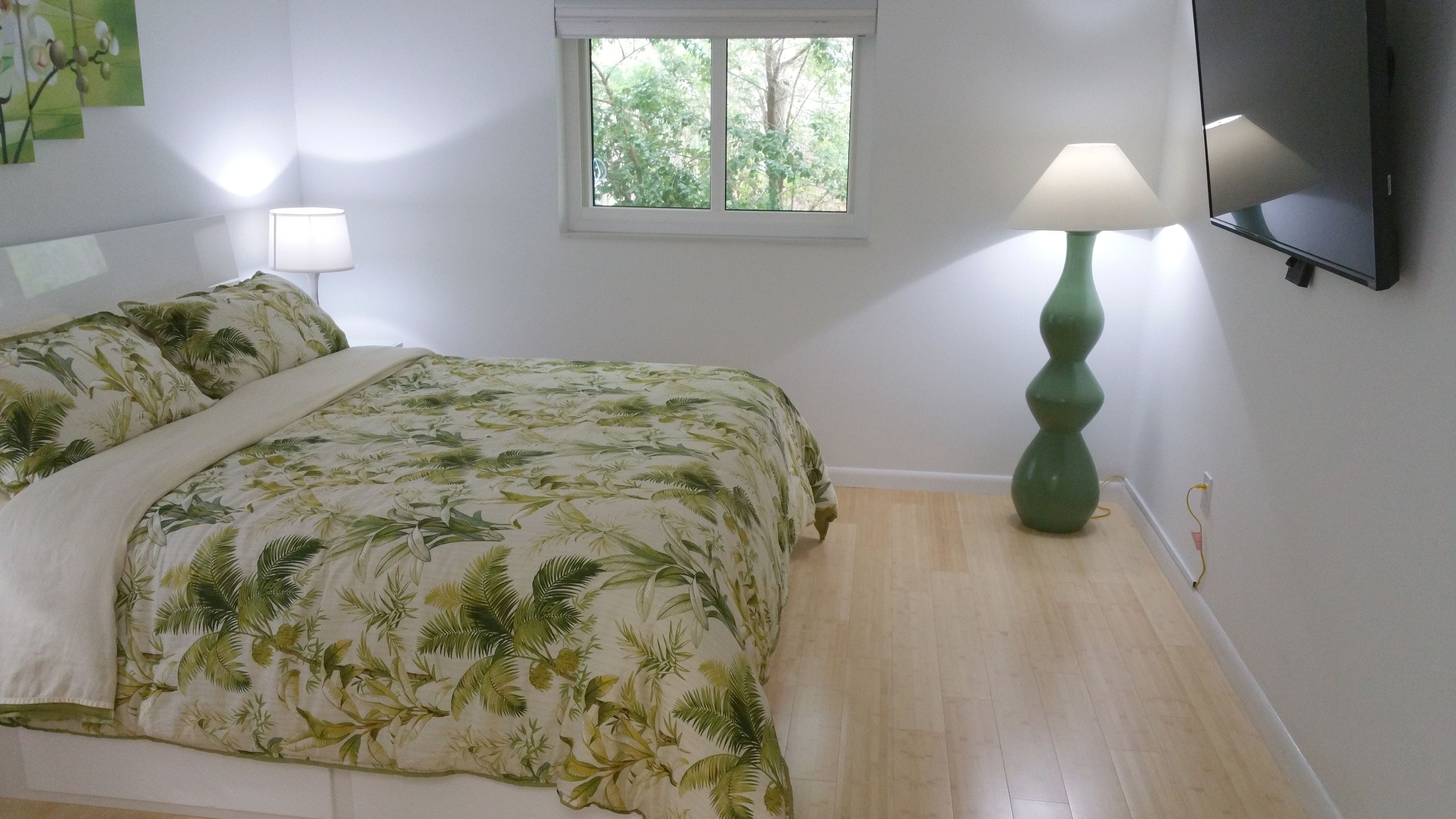 Ein Schlafzimmer mit Bett, Fenster, Lampe und Fernseher.