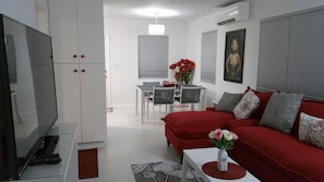 Uma sala de estar moderna com um sofá vermelho, uma televisão e uma área de refeições ao fundo.