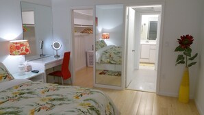 A bedroom with a bed, a desk with a mirror, a chair, a wardrobe, and a bathroom visible through an open door.