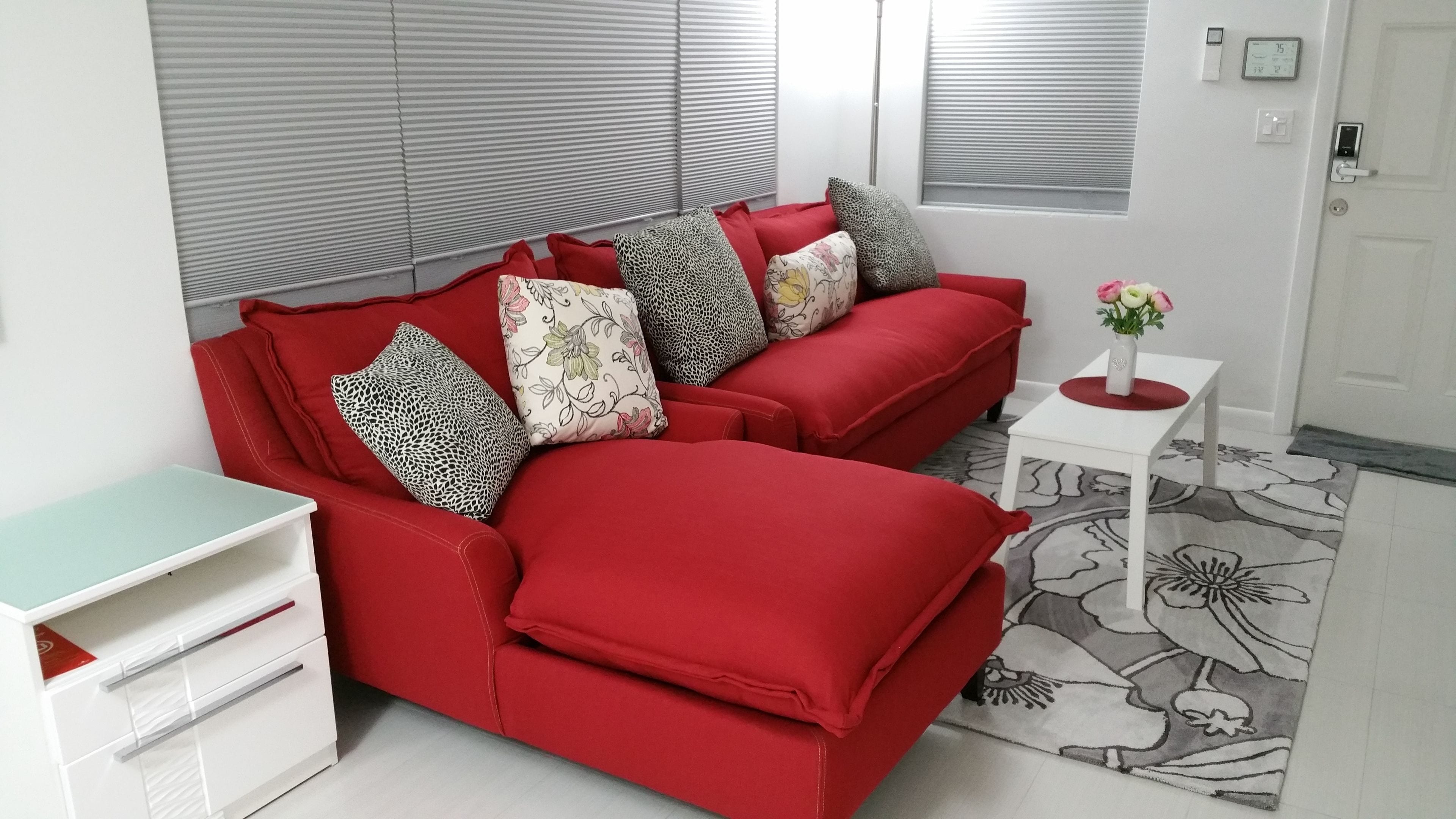 A red sofa with patterned cushions, a white side table with a vase, and a patterned rug.