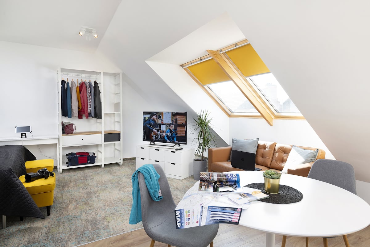 A modern living space with a loft bedroom, a dining area, and a TV in the background.
