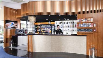 A modern reception area with a wooden reception desk, a self-service bar, and a display of magazines and books.