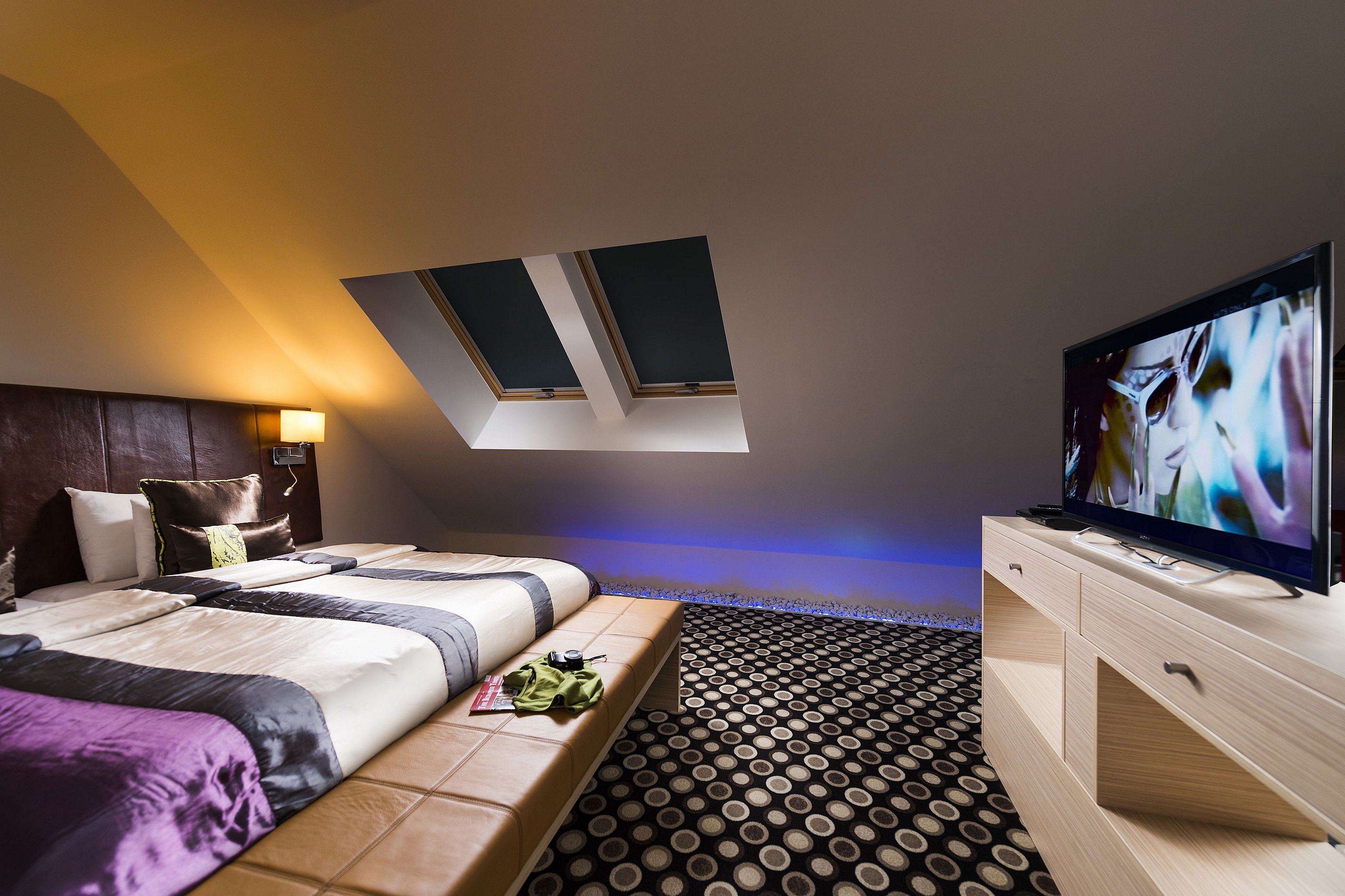 A modern hotel room with a bed, a TV, a desk, and a skylight.
