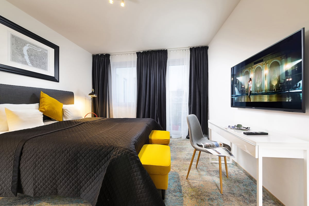 A hotel room with a bed, a desk, a chair, a TV, and a window with curtains.