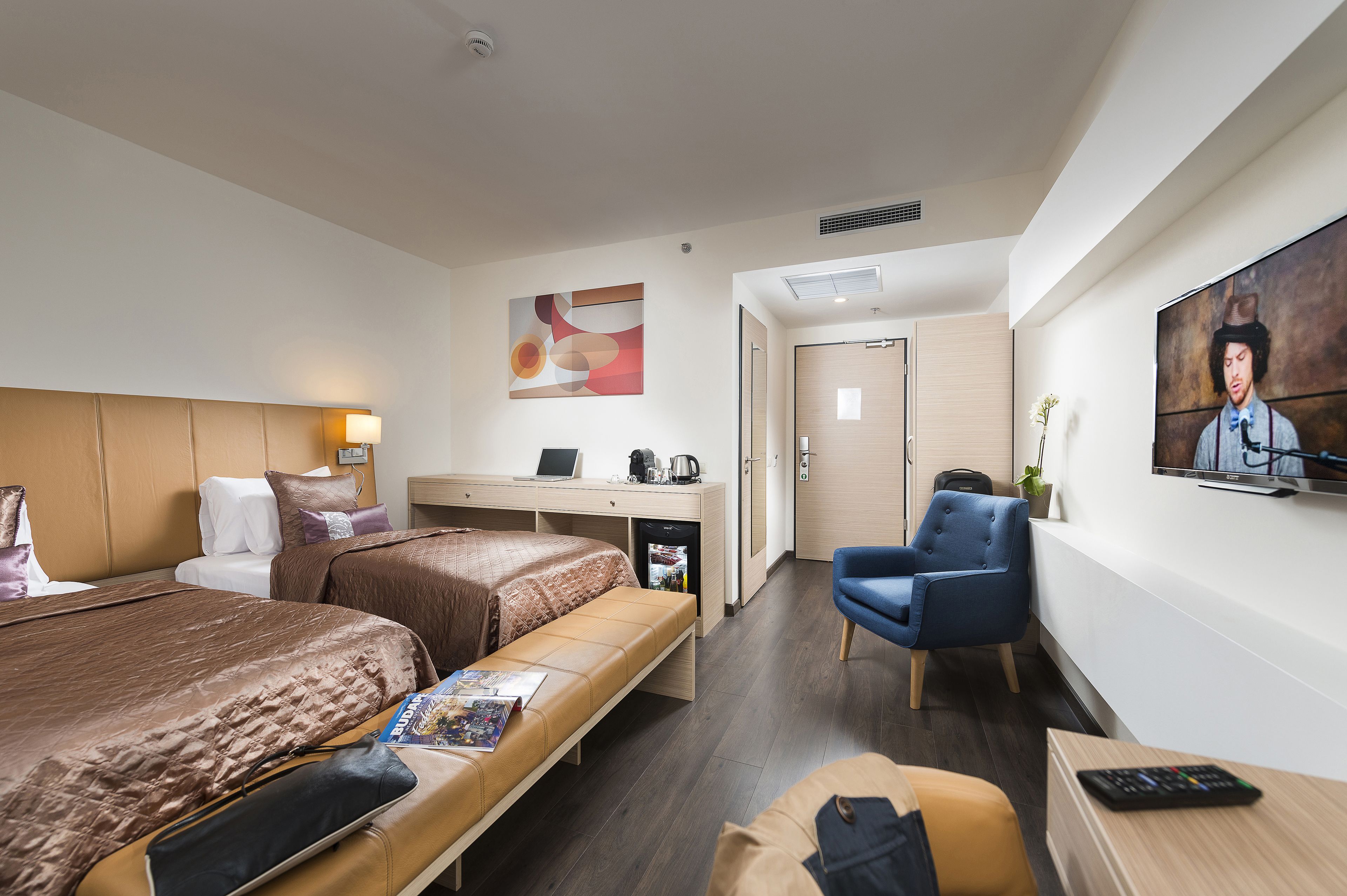 A hotel room with a bed, a desk, a chair, a TV, and a small table.