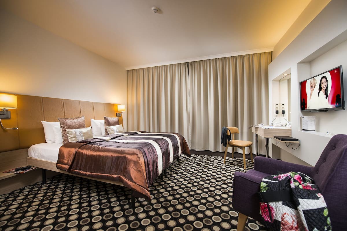 A hotel room with a bed, a desk, a chair, a television, and a patterned carpet.