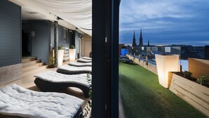 Ein modernes Hotelzimmer mit Balkon, Blick auf eine Stadtsilhouette und einer ordentlich eingerichteten Sitzecke mit Kissen.