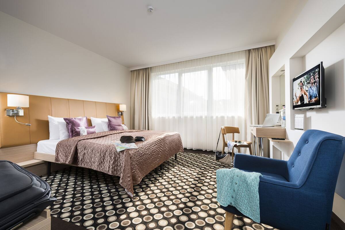A hotel room with a bed, a desk, a chair, and a television.