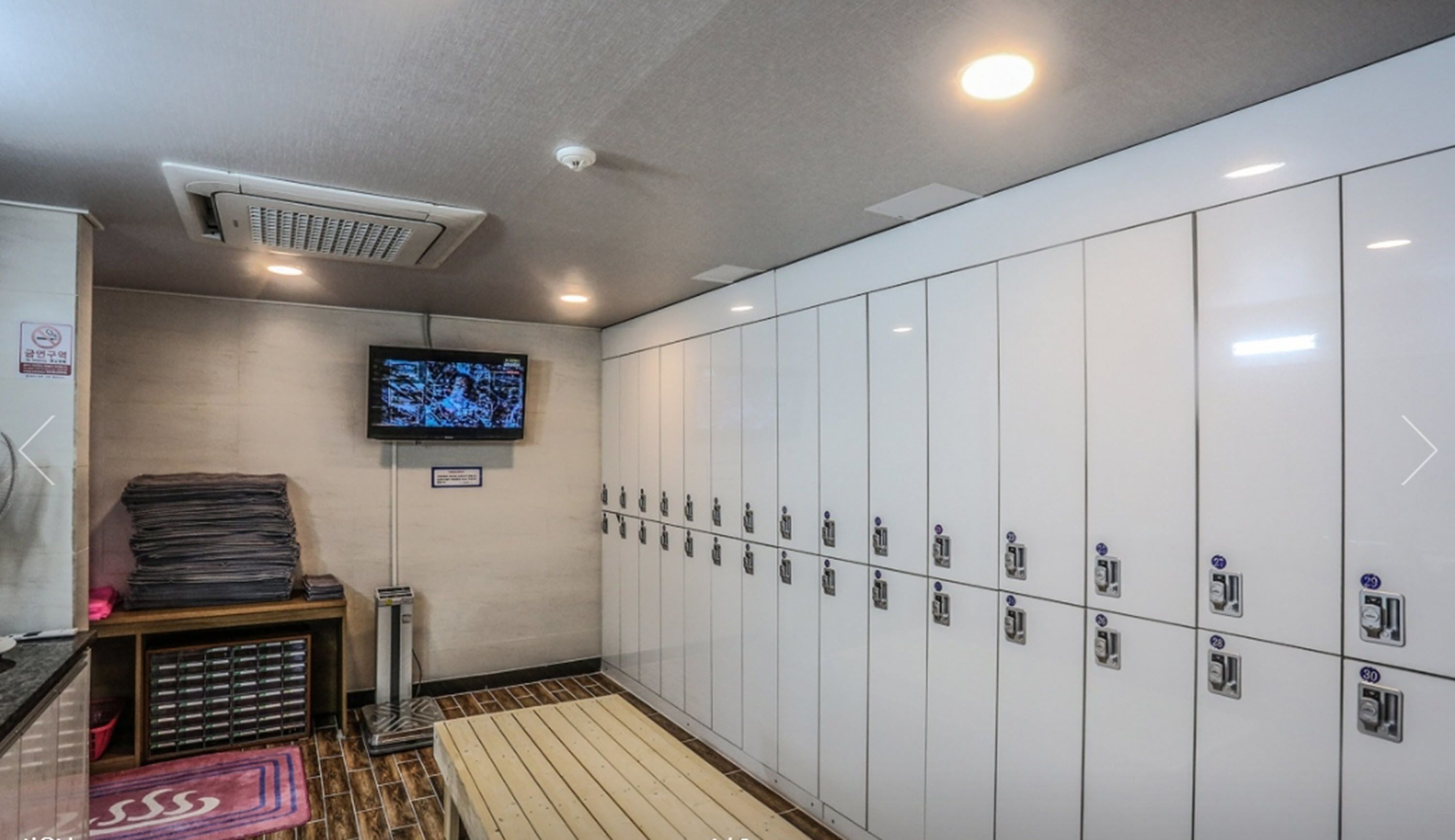 A locker room with a television mounted on the wall, a ventilation system, and a stack of magazines on a table.