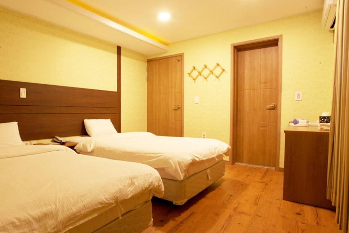 Habitación de hotel con dos camas, cabeceros de madera, un escritorio pequeño y un armario de madera.