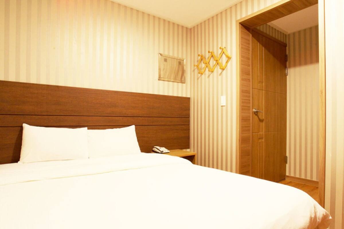 Habitación de hotel con una cama grande, cabecero de madera, papel tapiz a rayas, una mesita de noche con teléfono y un armario de madera.