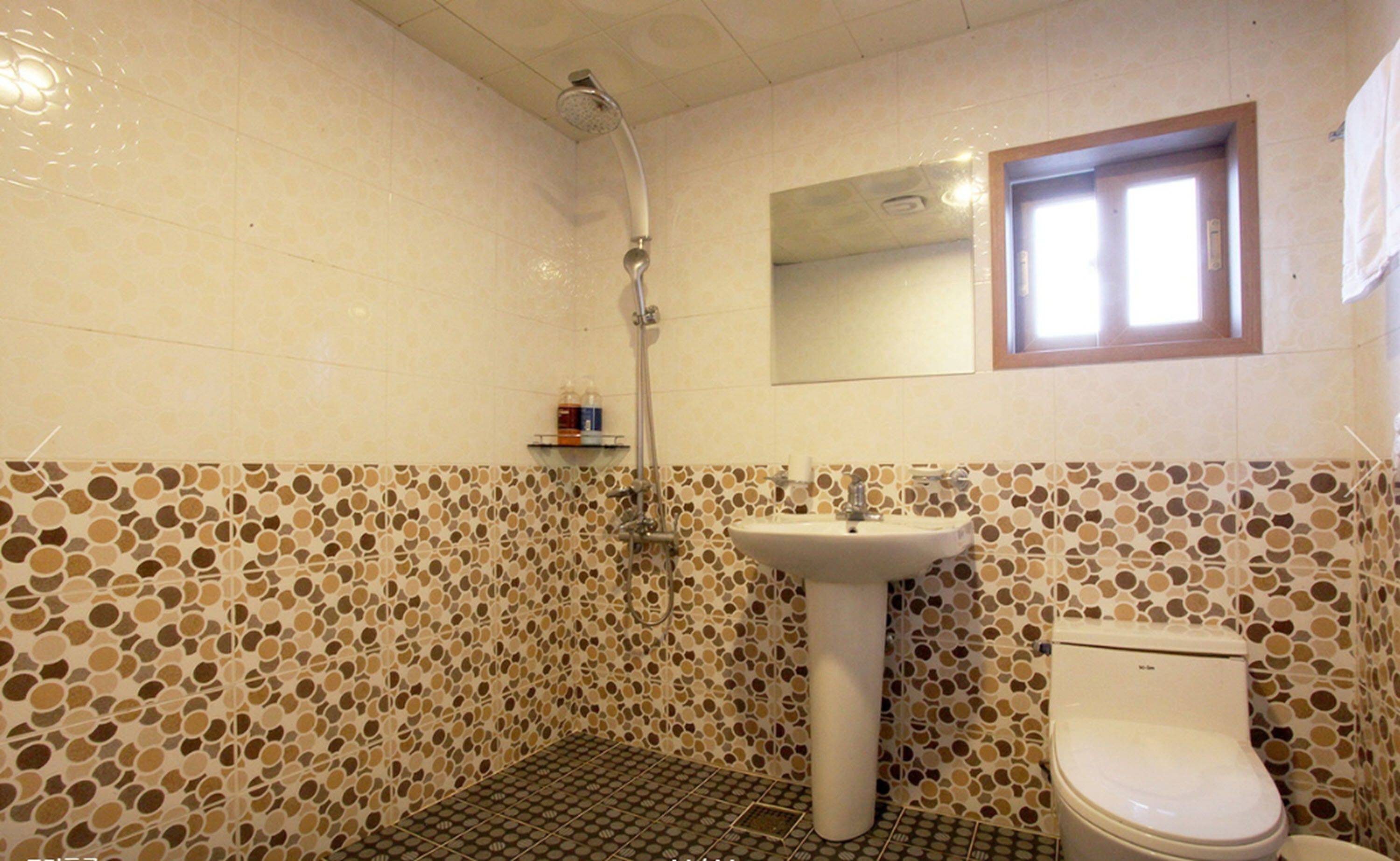 A bathroom with a toilet, sink, and shower. The walls have a mosaic tile pattern.