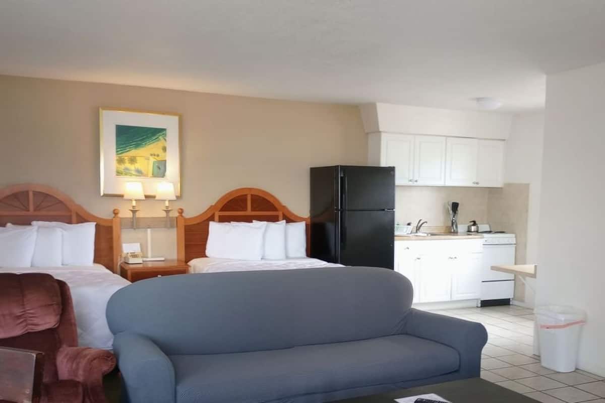 A hotel room with a bed, a sofa, a kitchen area with cabinets and a refrigerator, and a trash bin.