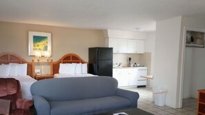 A hotel room with a bed, a sofa, a kitchen area with cabinets and a refrigerator, and a trash bin. - Ocean Court Beachfront Hotel (Daytona Beach Shores)