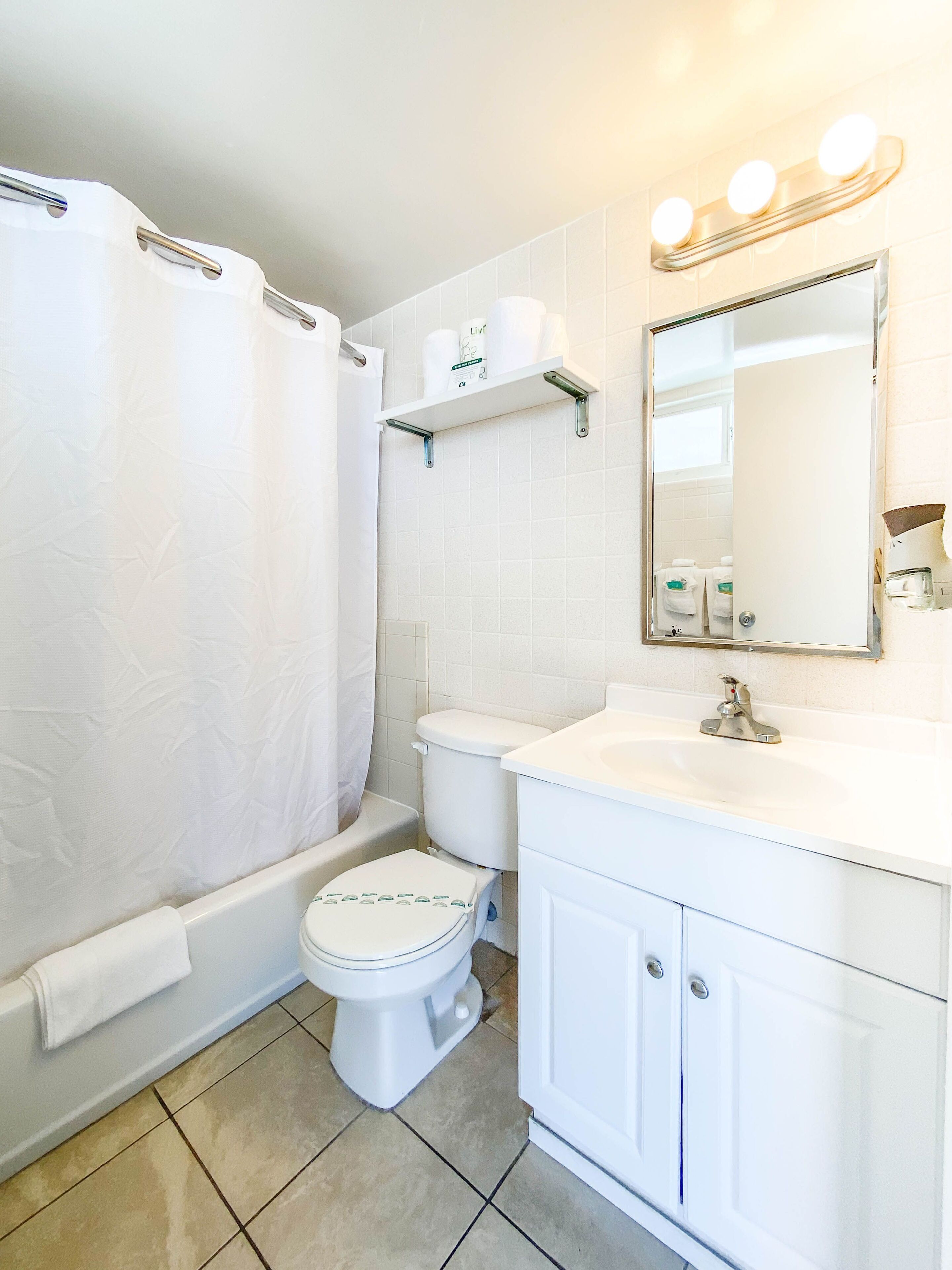 A bathroom with a toilet, a shower curtain, a sink, and a mirror with lights.