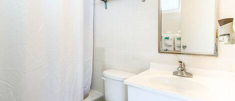 A bathroom with a toilet, a shower curtain, a sink, and a mirror with lights.