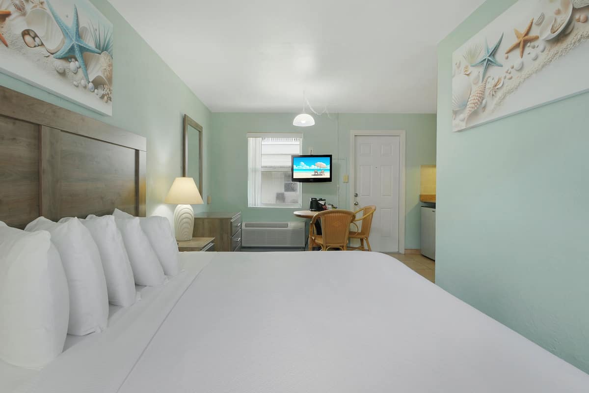A hotel room with a large bed, a desk with a chair, a television, and a window.