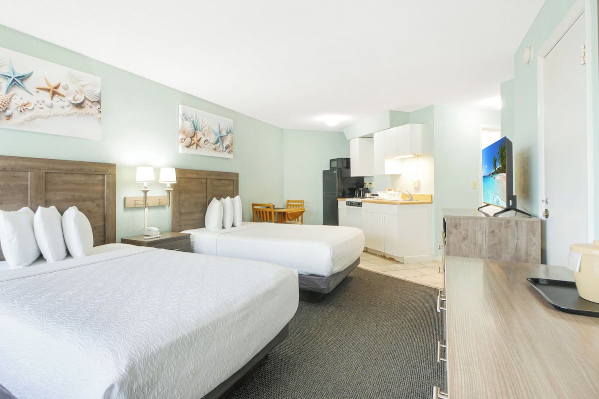 A hotel room with two beds, a kitchenette, a dining area, and a TV.