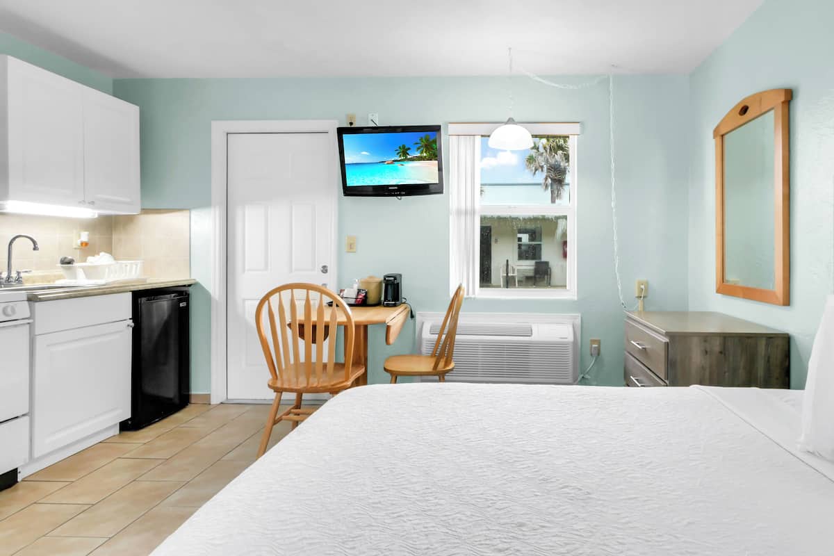 A hotel room with a bed, a desk, a chair, a TV, and a window with a view of palm trees.