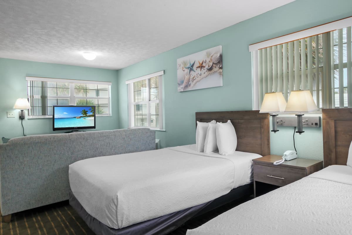 A hotel room with two beds, a television, a desk with a lamp, and a window with blinds.