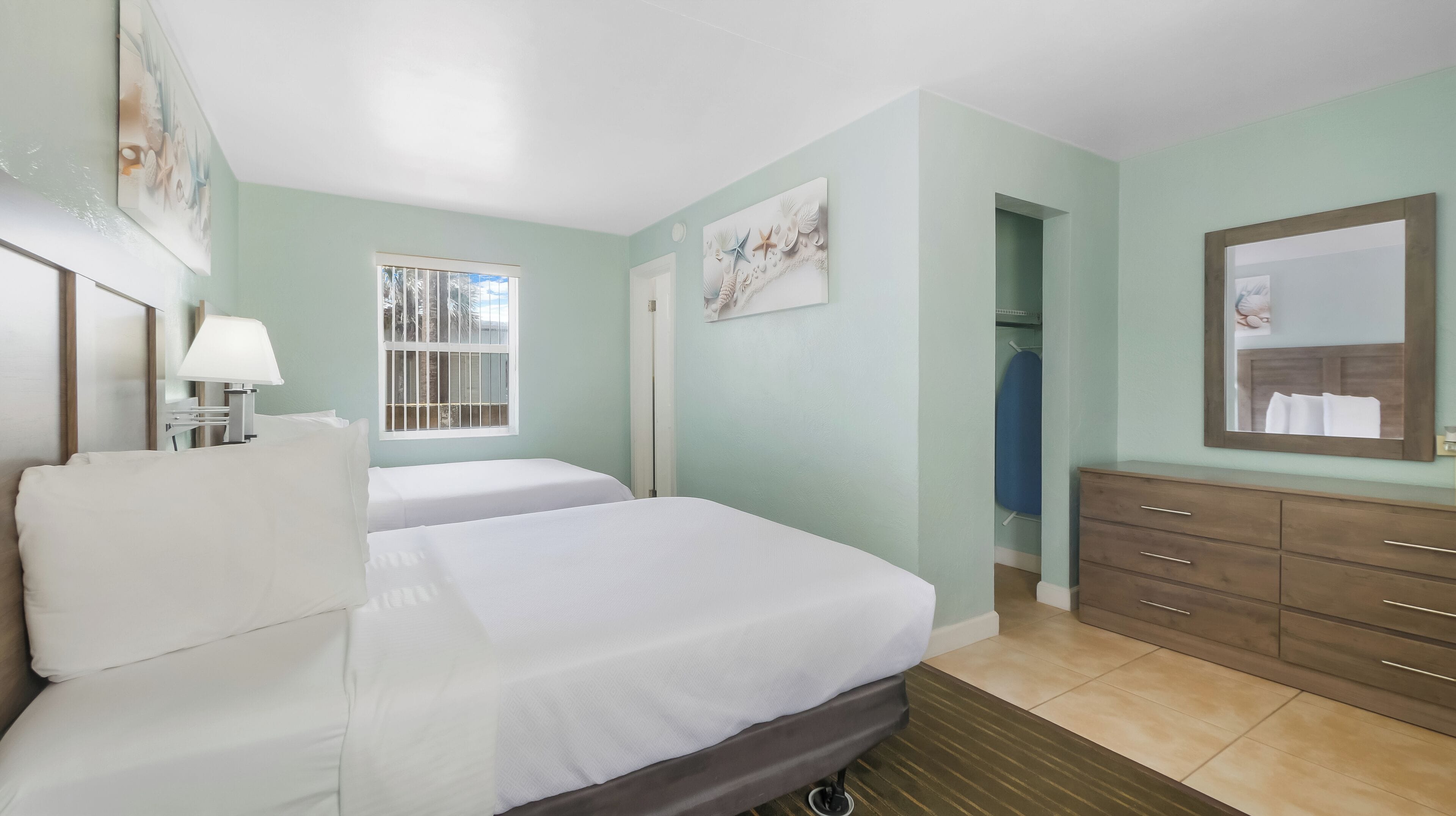Quarto de hotel com duas camas, penteadeira, espelho e obras de arte nas paredes.