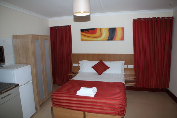 A hotel room with a bed, a desk, a wardrobe, and a painting on the wall.
