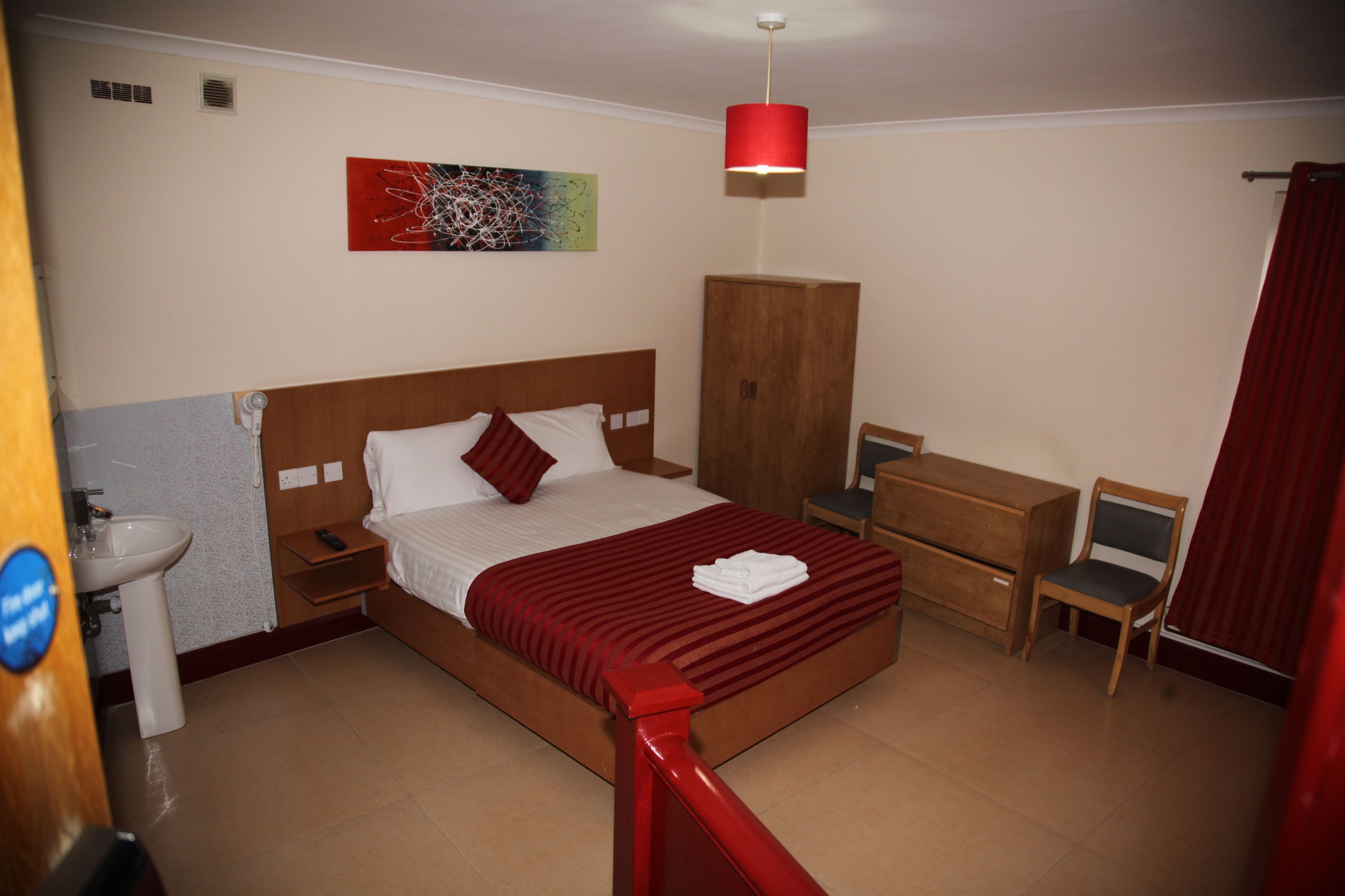 Habitació d'hotel amb llit, escriptori, cadira, armari i cortina vermella.