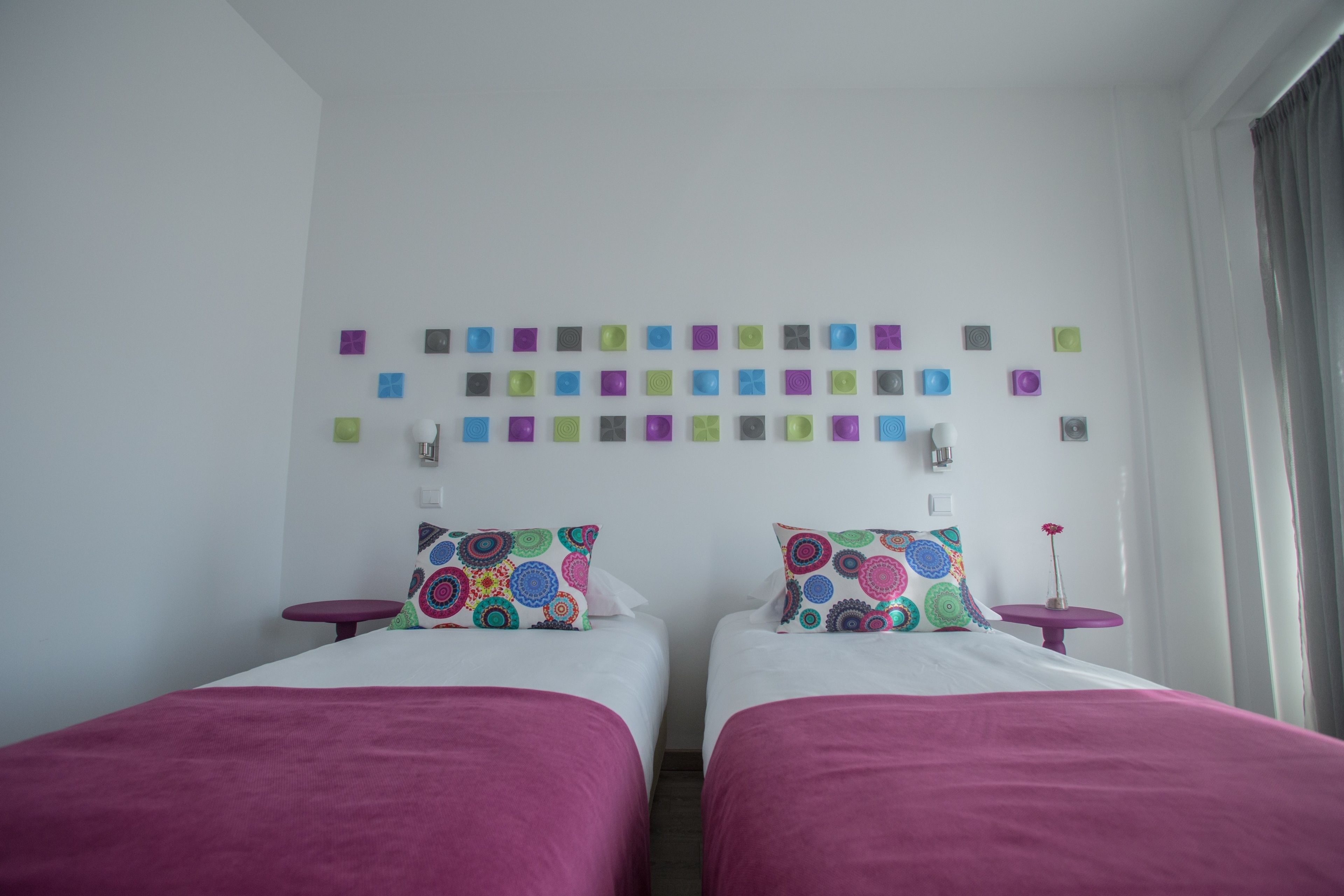 A hotel room with two beds, a wall-mounted light fixture, and a small table with a vase.