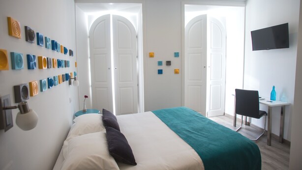 Una habitación de hotel con una cama, un escritorio, una silla, un televisor y obras de arte en la pared.