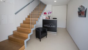 Un interior moderno con una escalera de madera, una recepción y un sillón negro.