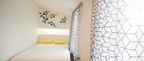 A bedroom with a bed, a headboard with wall decals, and a geometric-patterned curtain.