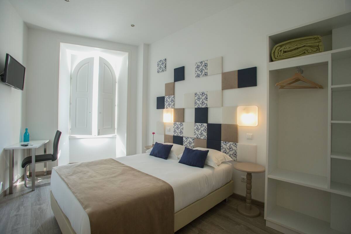 A hotel room with a bed, bedside table, chair, desk, and a wardrobe.