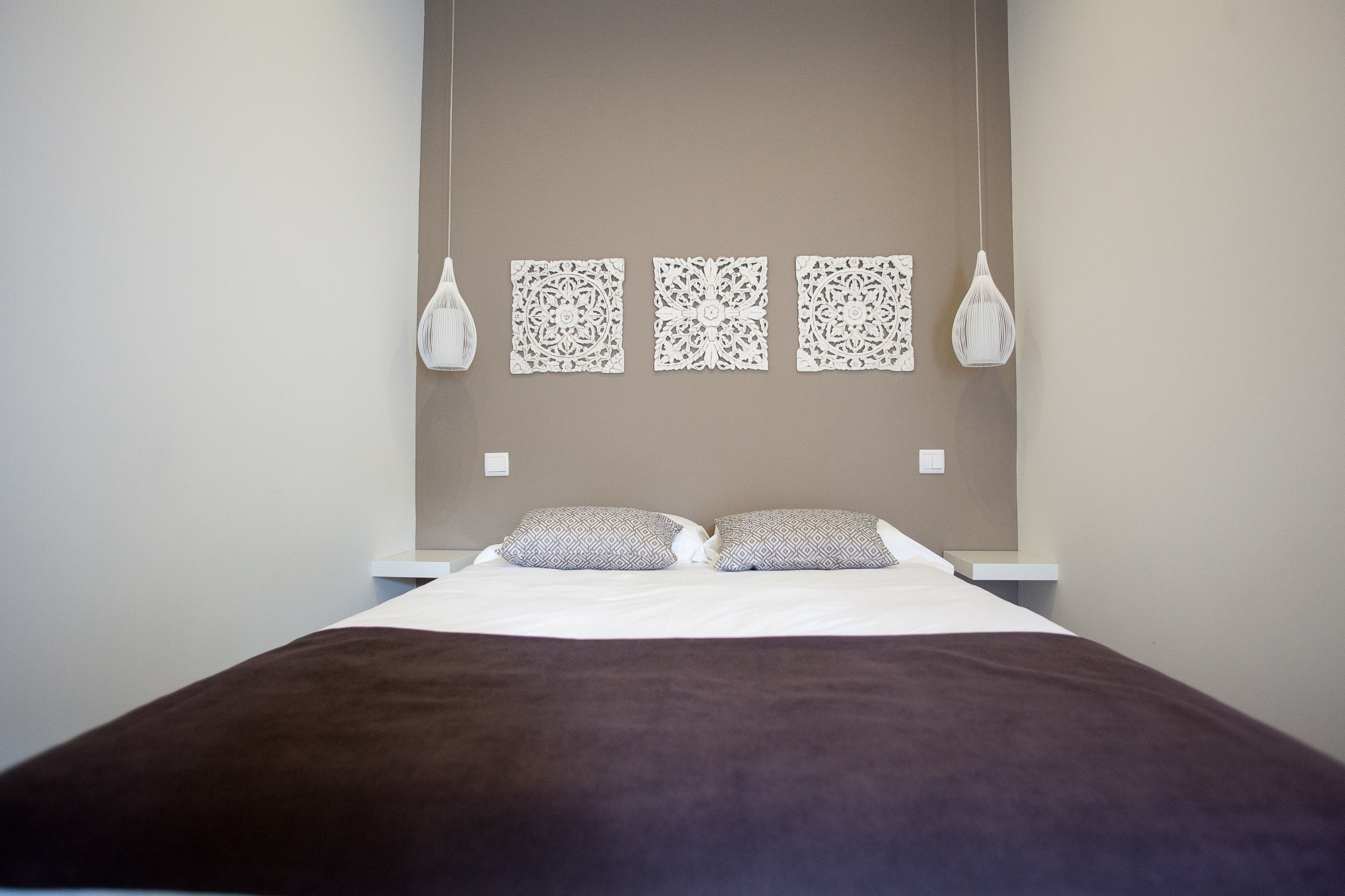 Una cama bien hecha con una manta marrón, dos almohadas y tres paneles decorativos en la pared.