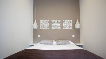 Una cama bien hecha con una manta marrón, dos almohadas y tres paneles decorativos en la pared.
