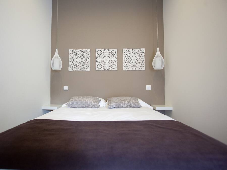 Cama bem arrumada com manta marrom, dois travesseiros e três painéis decorativos fixados na parede.
