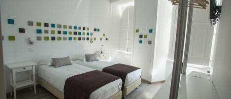 Un dormitorio con dos camas, una mesita de noche, un armario y una pared decorada con cuadrados de colores.