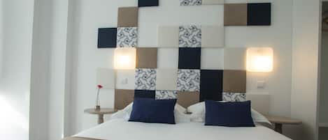 A hotel room with a bed, two bedside tables, and a wall-mounted light fixture.