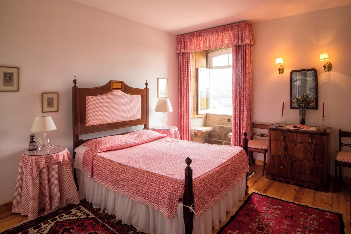Un dormitorio con una cama de madera, dos mesitas de noche con lámparas, un aparador y dos alfombras.