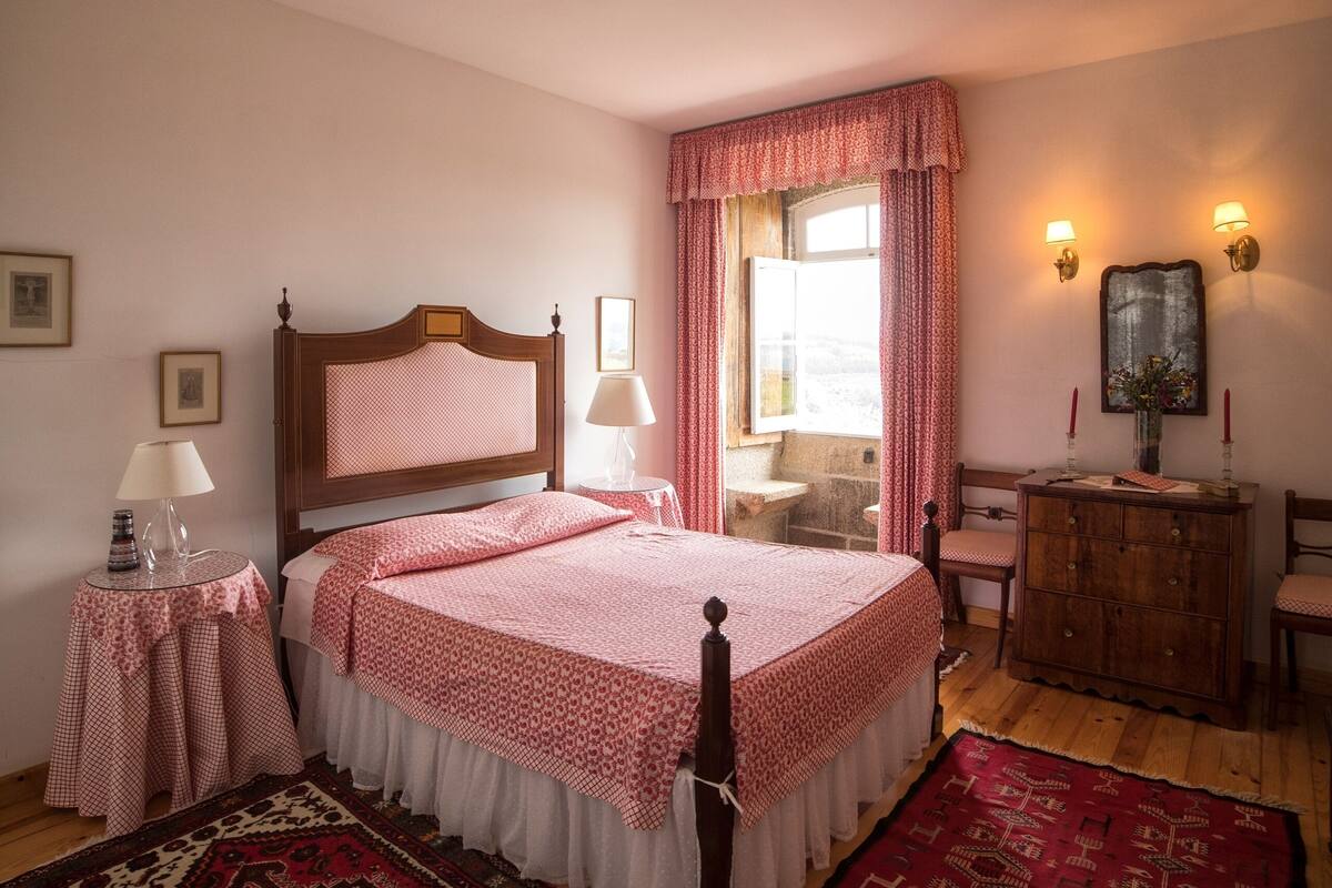 A bedroom with a wooden bed, two bedside tables, a dresser, and a window with curtains.