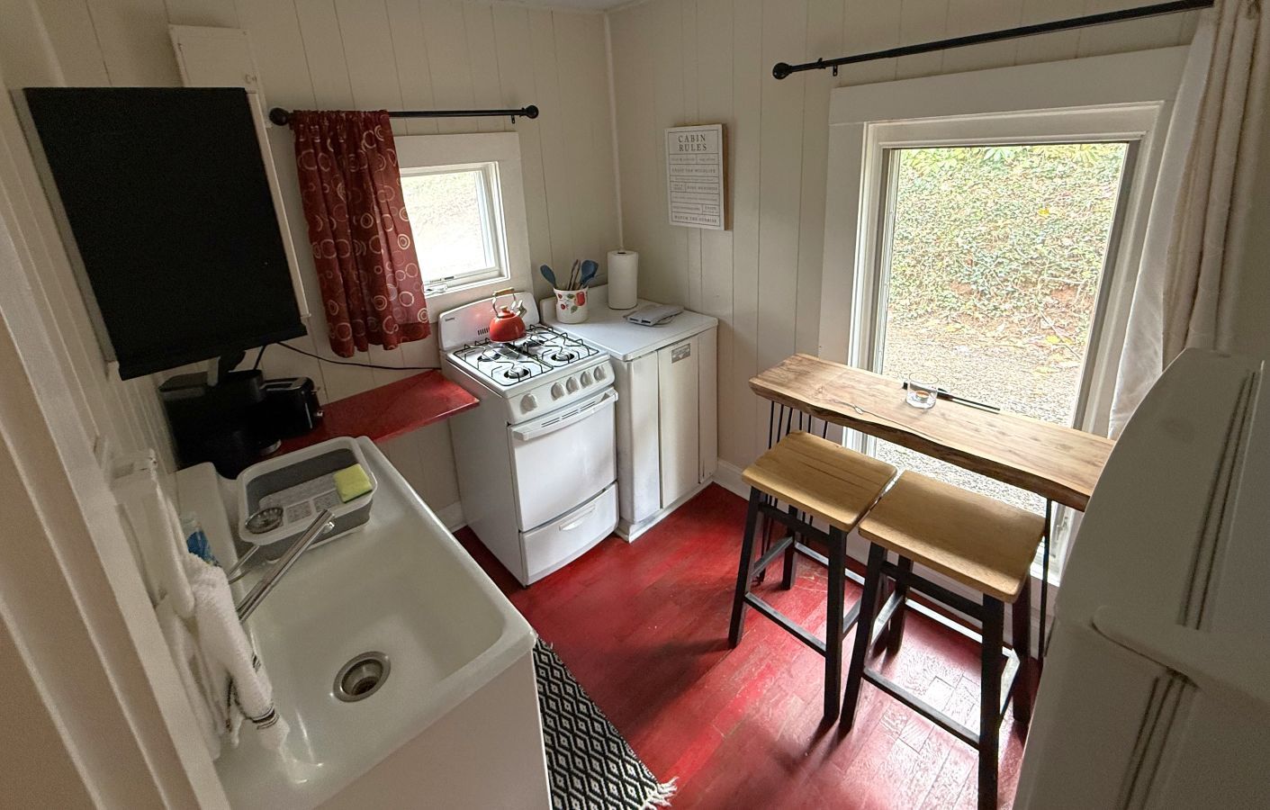 Una cocina funcional con estufa, lavamanos y un pequeño comedor con taburetes.
