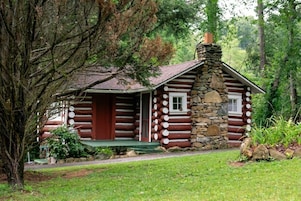 Une cabane en rondins avec une cheminée en pierre, une véranda et une petite fenêtre.