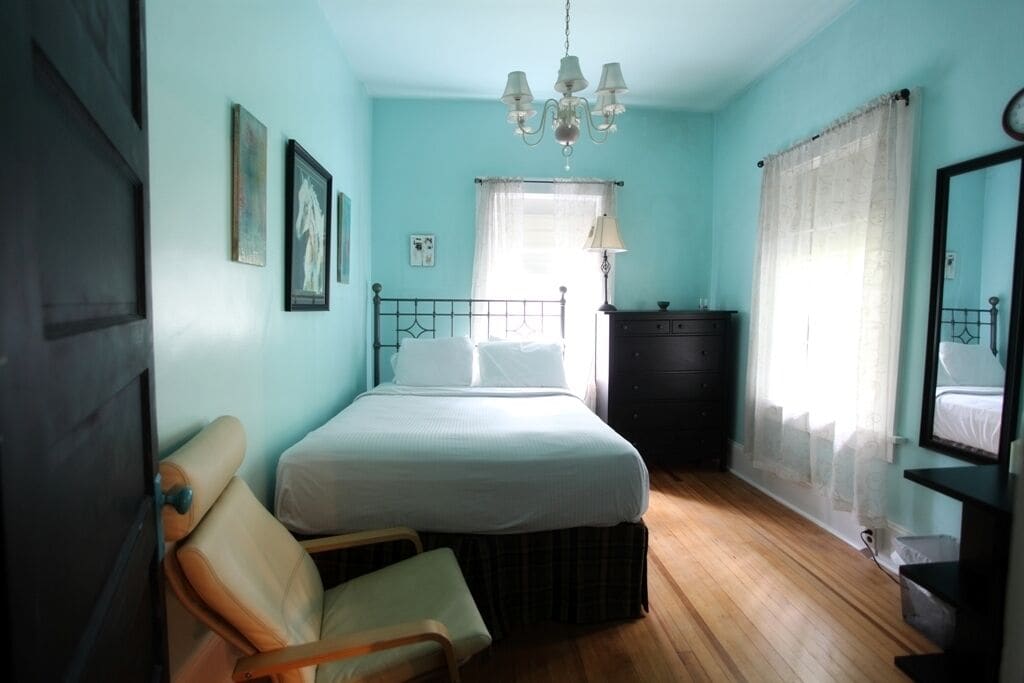 A bedroom with a bed, a chair, a dresser, and a mirror.