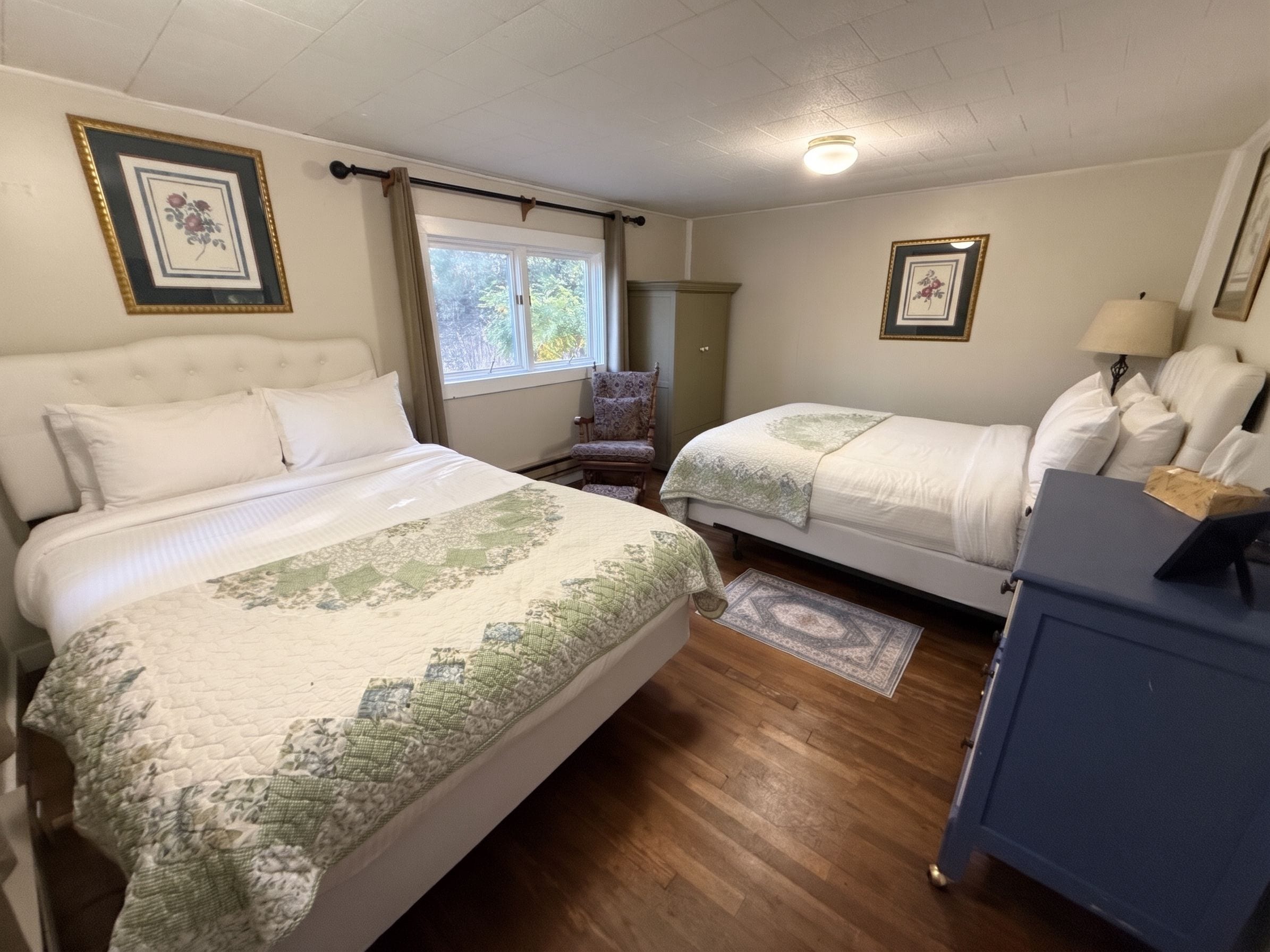 A bedroom with two beds, a chair, a desk, and a window.