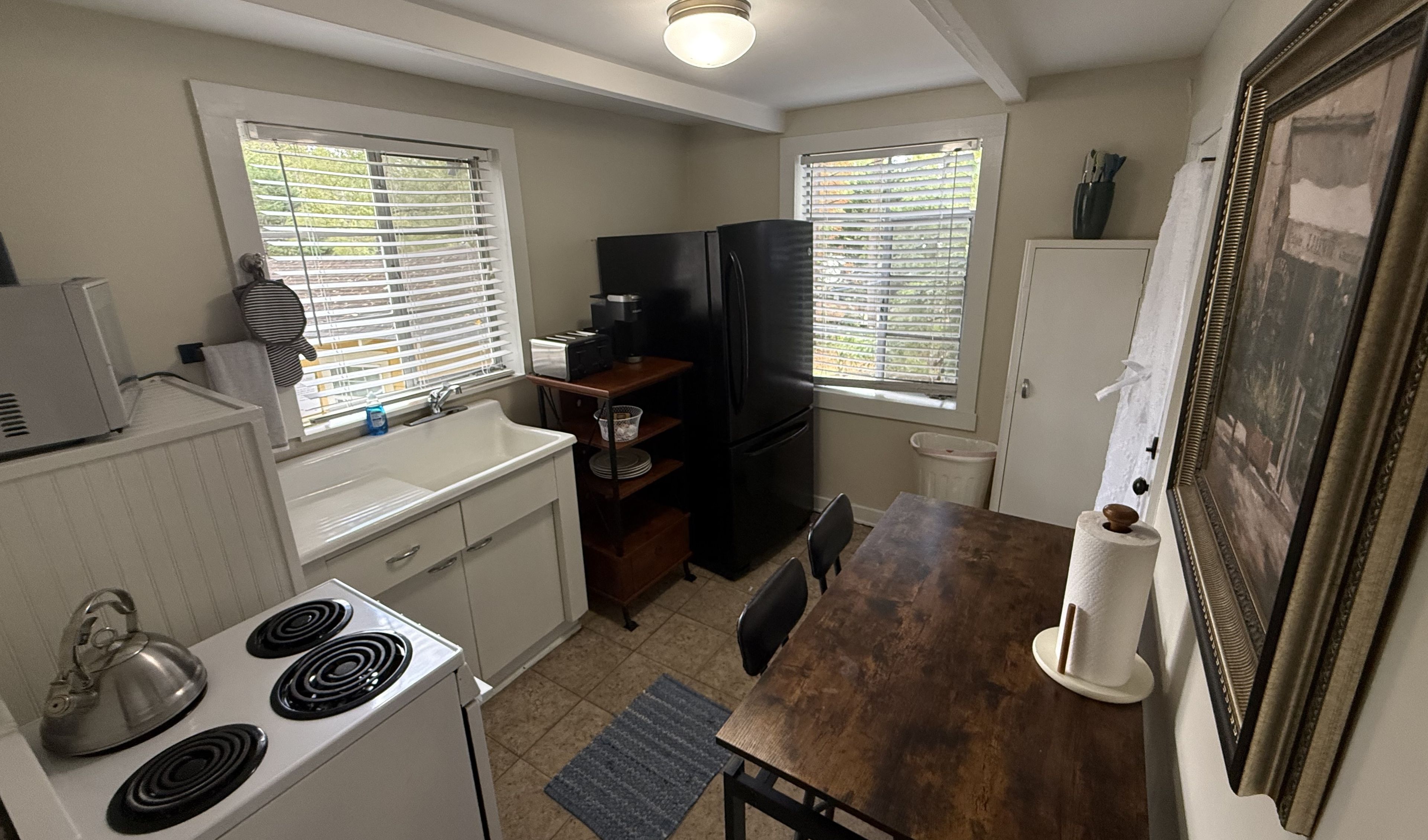 A compact kitchen with white cabinets, a stove, a refrigerator, and a dining table.