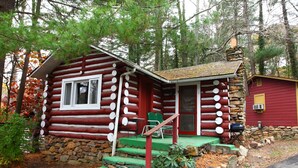 A log cabin with a stone foundation, a porch with green steps, and a red exterior. - The Pines Cottages (Asheville)