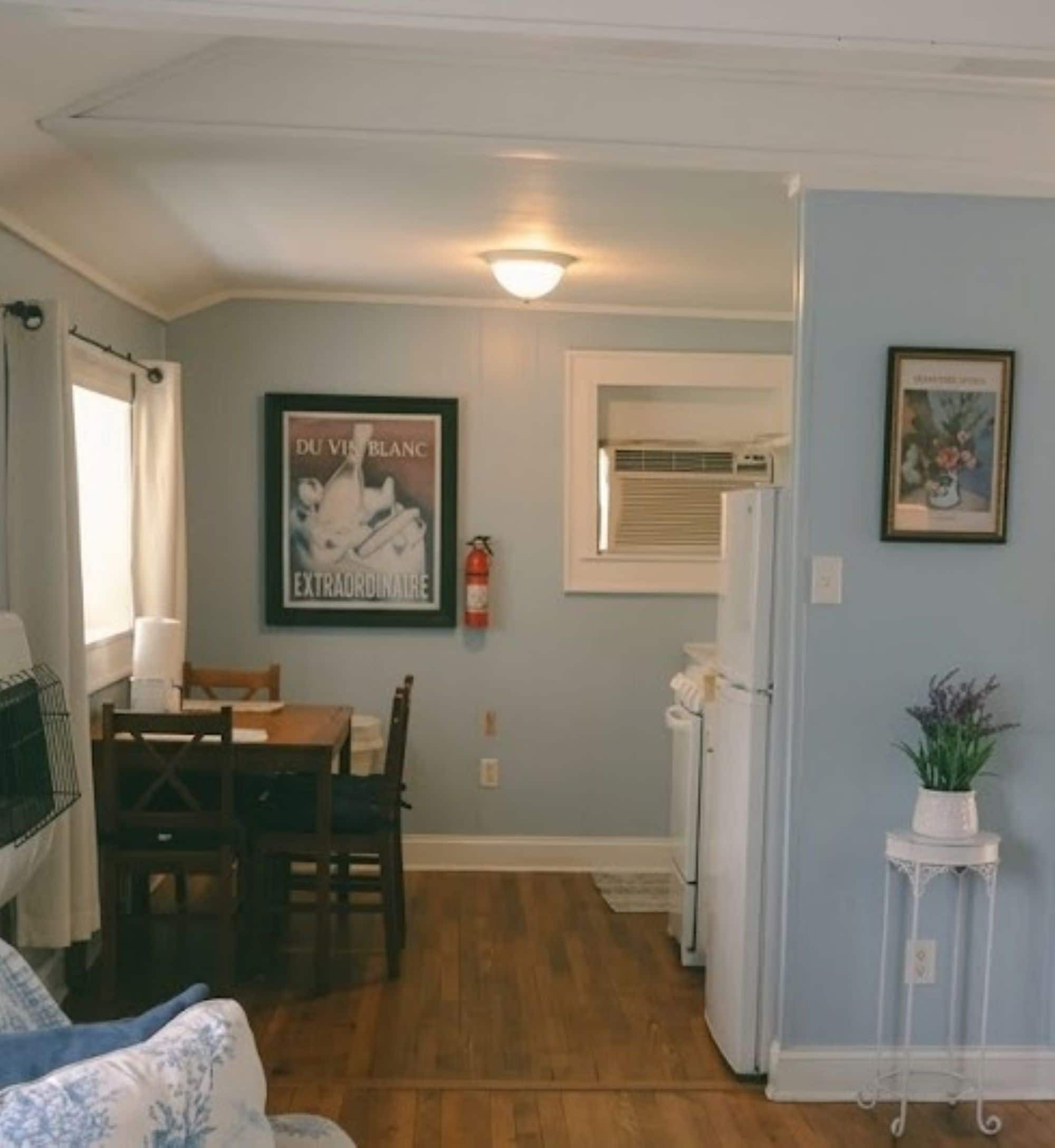 Una habitación con una mesa de comedor, sillas, un cuadro enmarcado, un radiador blanco y una ventana con cortinas.
